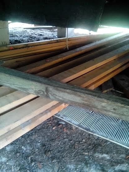 A bunch of wooden boards are laying on the ground under a building.