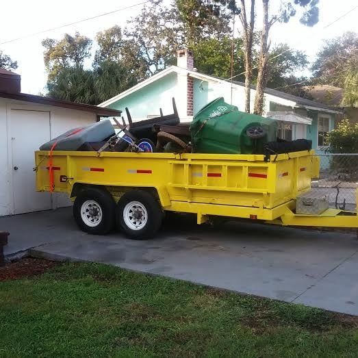 A yellow trailer filled with garbage is parked in front of a house.